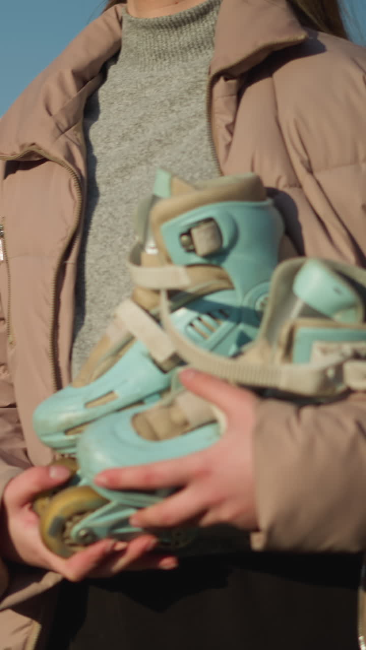 una chica caminando en un día soleado mientras sostiene una patineta con ambas manos. está vestida con una chaqueta de melocotón y una camisa interior gris, mirando hacia adelante mientras se pasea por un ambiente exterior brillante