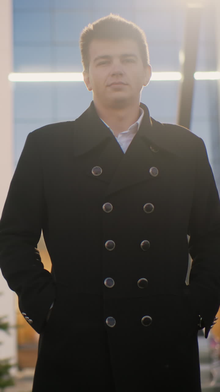 검은 코트를 입은 쇼핑몰 소유자가 주머니에 손을 넣고 쇼핑몰 앞에 서 있습니다. 스포츠 재미있는 모습, 배경에는 거리 조명과 주차된 자동차, 캐주얼하고 경쾌한 표정이 있습니다.