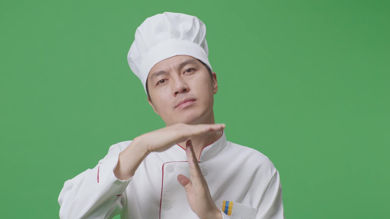 Close Up Of Asian Man Chef Looking At Camera And Showing Time Out Hands Gesture While Standing In The Green Screen Background Studio