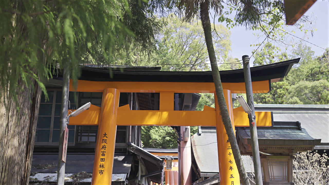 Tranquil pathway lined with vibrant red gates in a beautiful forest environment. Shrine text translation: ''Tondabayashi City, Osaka Prefecture''. Kyoto, Japan, Fushimi Inari