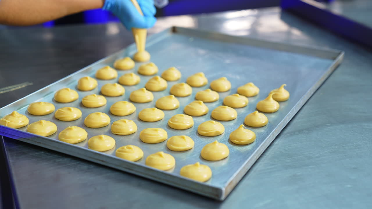 Confectioner in gloves squeezes liquid batter on the baking sheet. Sweets manufacturing at confectionary factory.