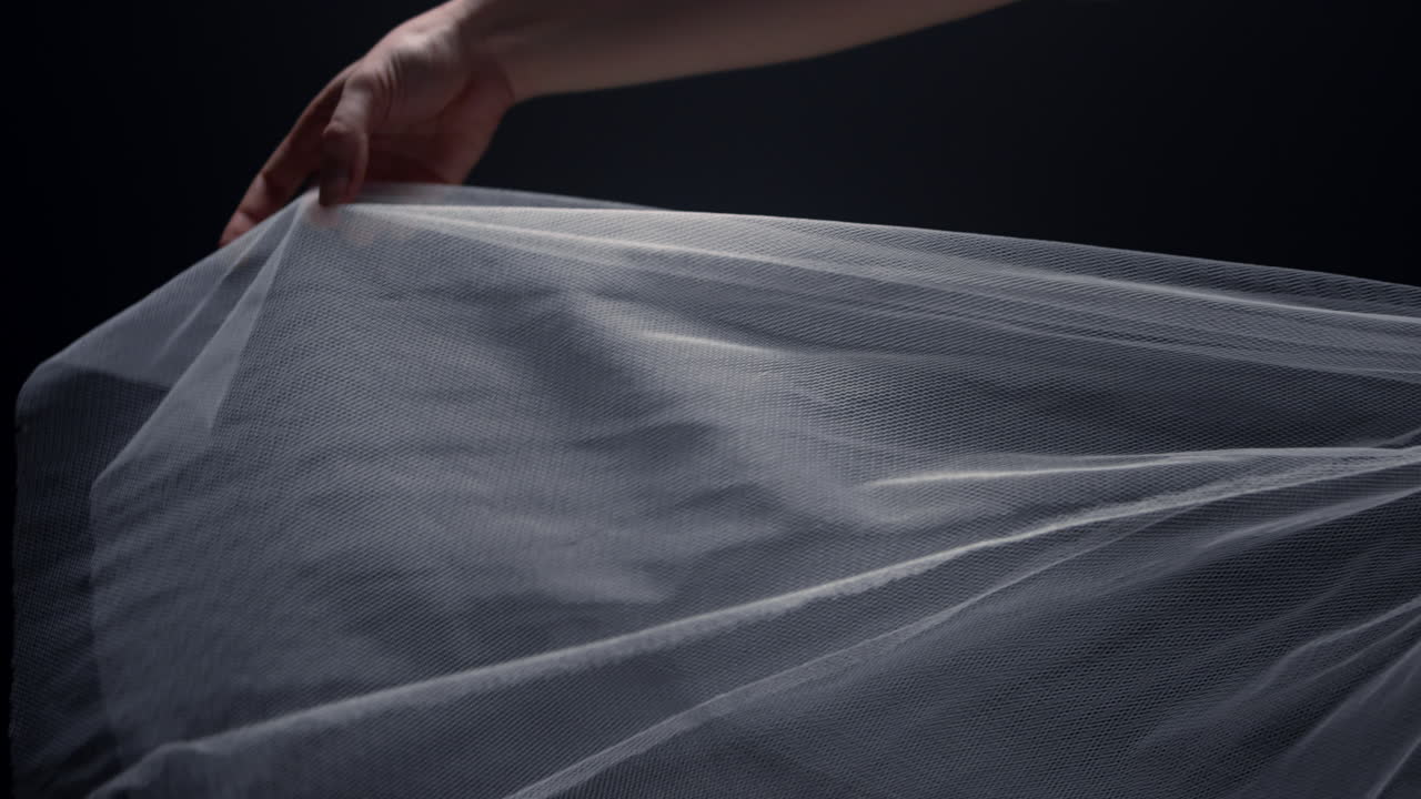 발레리나의 팔이 실내에서 투투 스커트를 만지고 댄서의 손이 드레스 헤임으로 놀고 있습니다.