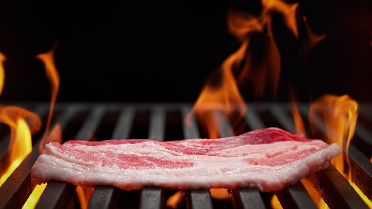 Bacon Falls Onto Charcoal Grill on the Black Background, Flames Burst From Beneath The Grill Grate in Slow Motion