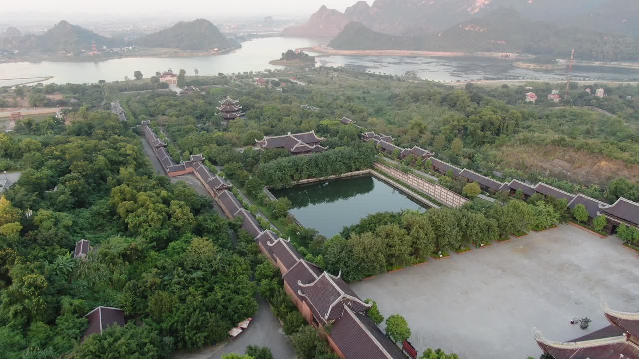 vista aérea de un avión no tripulado en vietnam volando sobre una zona de templo budista llena de árboles verdes frente a un río serpiente en ninh binh al atardecer
