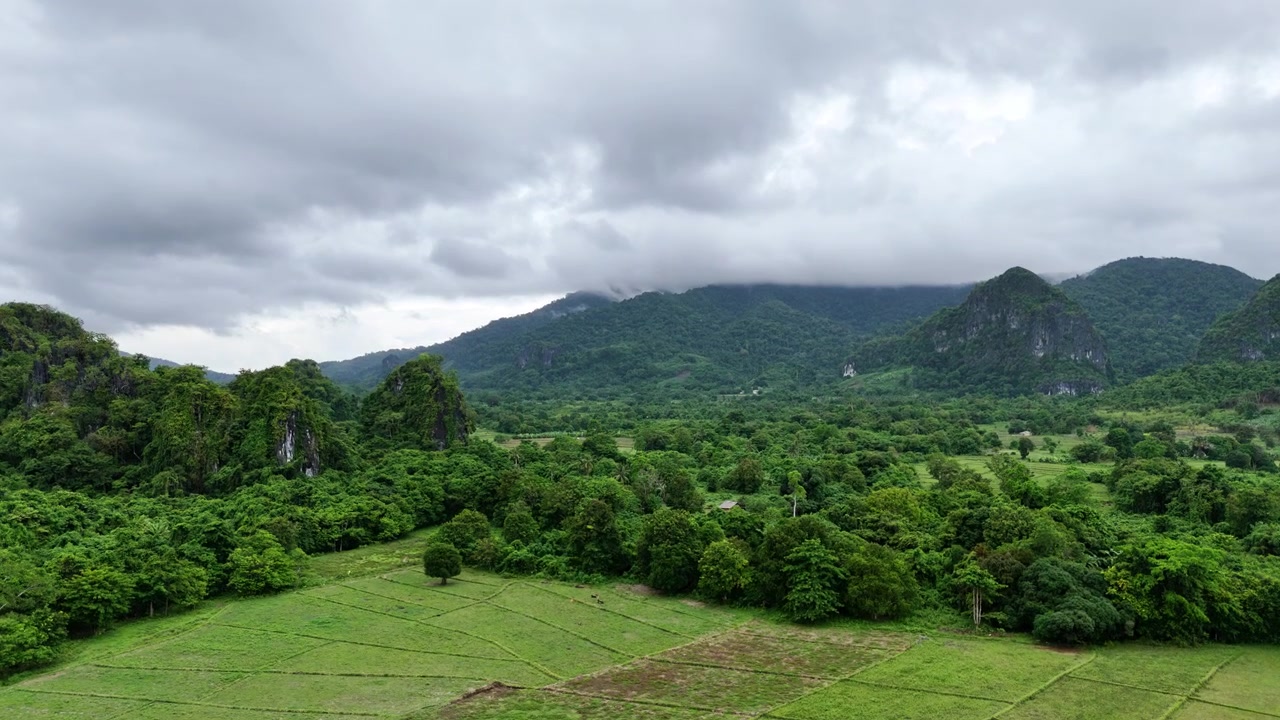 Vista aérea de drone dos arrozais verdes no Vale Dewil, ladeados por afloramentos cársticos de calcário e cristas de montanhas cobertas de nuvens sob céus tempestuosos, New Ibajay, El Nido, Palawan, Filipinas