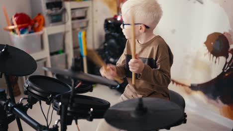 A-small-talented-albino-boy-with-white-hair-in-round-blue-glasses-energetically-plays-on-an-electronic-music-installation-using-wooden-sticks-during-his-weekend-rest-and-development-of-his-talent-and-hobby