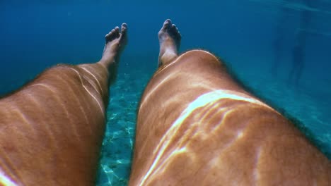 underwater personal perspective view of man legs floating in clear transparent sea water beneath surface with blue background