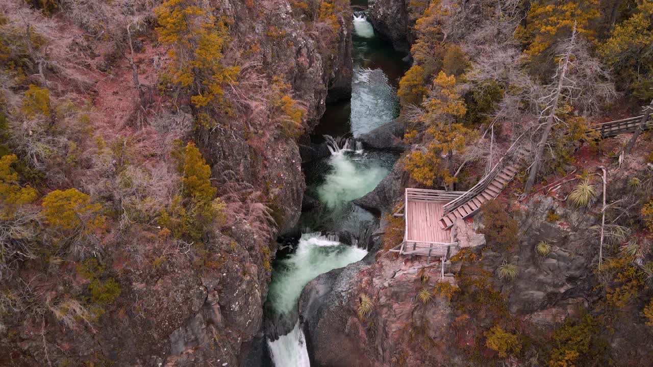 Tilting down drone aerial of waterfalls with viewing boardwalk, Siete Tazas National Park, Ñuble, Chile with emerald pools and autumn forest