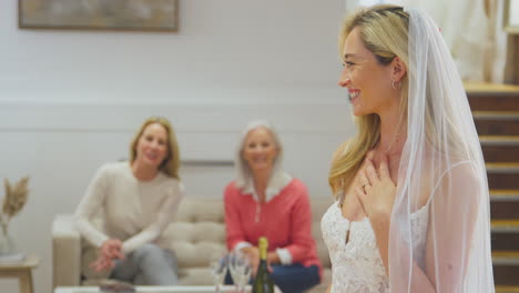 abuela con madre viendo a su hija adulta elegir y probarse el vestido de novia en la tienda de novias