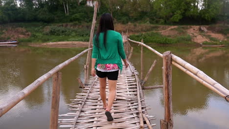 woman walking across a bamboo bridge over a river