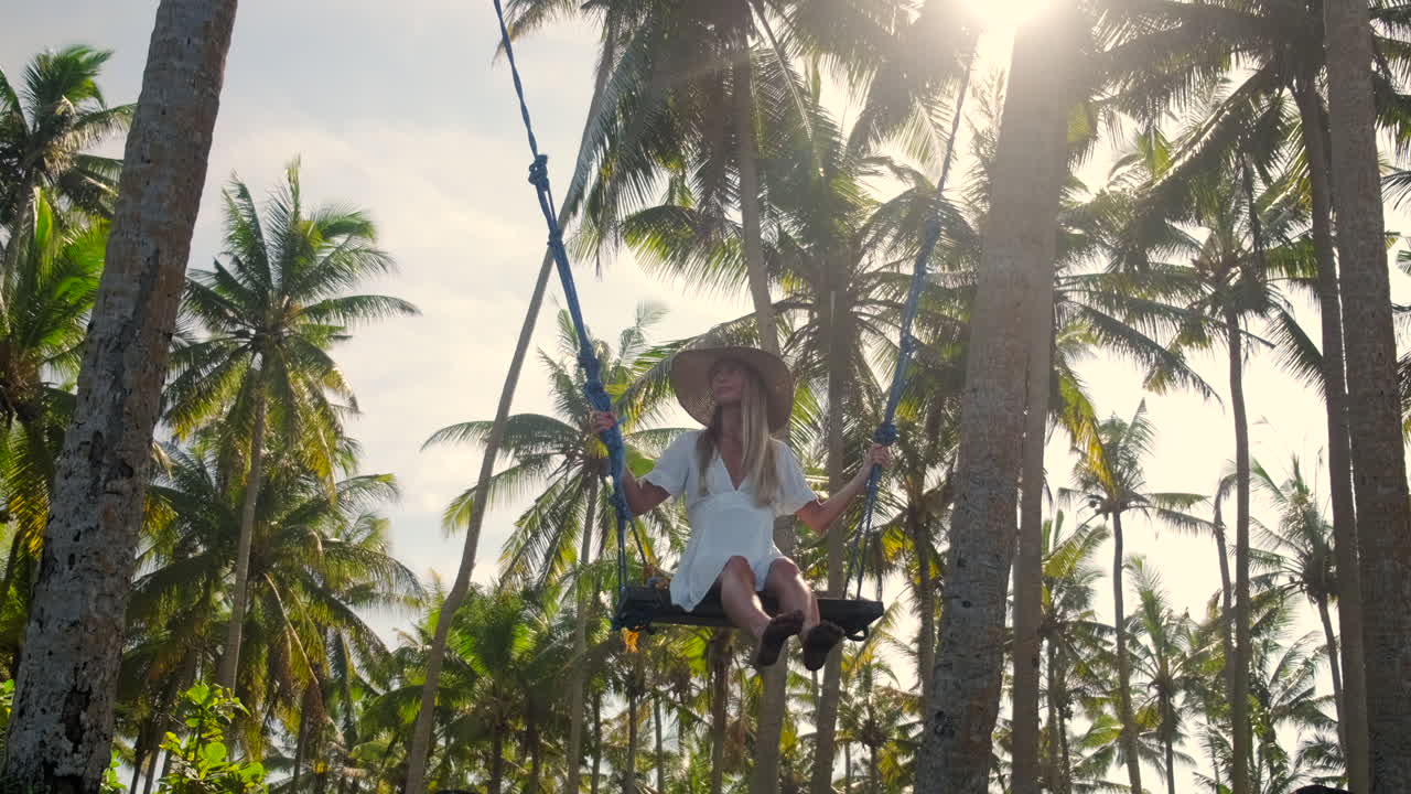 mujer disfrutando de un columpio en un palmeral tropical