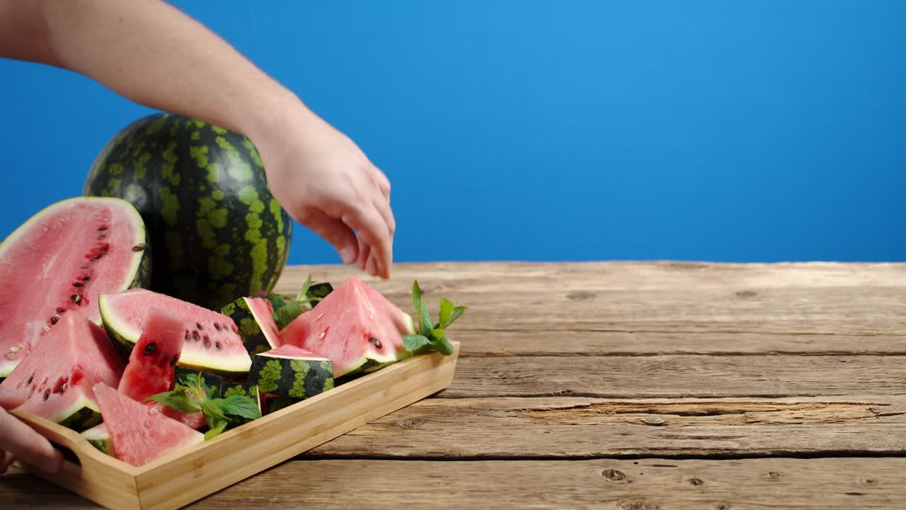 남자는 손으로 테이블에 수박 조각을 넣은 트레이를 놓았습니다.