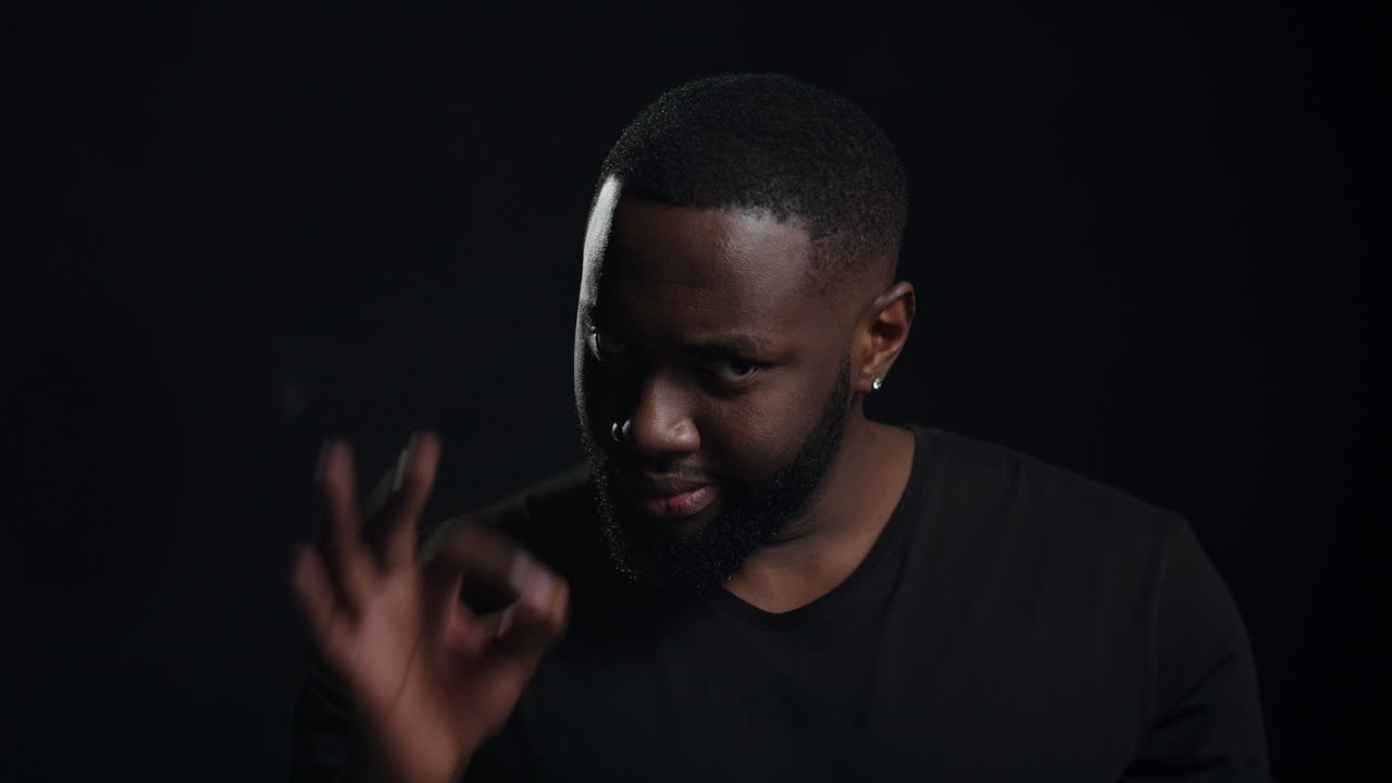 Unpredictable afro guy showing ok sign indoors. Emotional man posing in studio