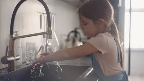 una niña en edad preescolar se está lavando las manos en la cocina después de cocinar. la hija está ayudando en la casa.