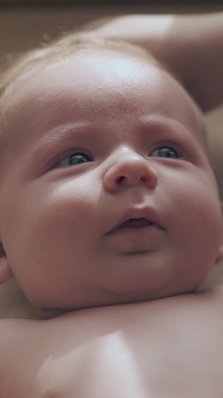 cute newborn boy with short fair hair and big crystal blue eyes lies on table and mother strokes blond head close view