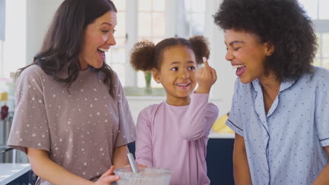 Family-With-Two-Mums-Wearing-Pyjamas-Making-Morning-Pancakes-In-Kitchen-At-Home-With-Daughter