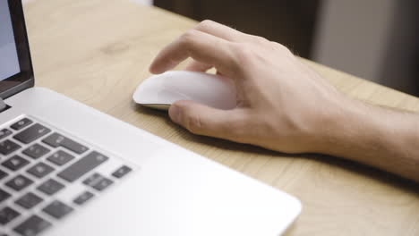 Toma-Cercana-De-La-Mano-Masculina-Joven-Usando-El-Mouse-Blanco-Al-Lado-De-La-Computadora-Portátil-En-La-Mesa