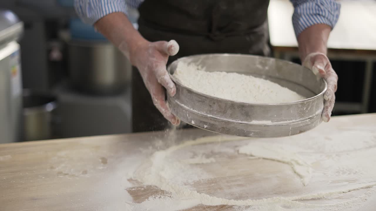 Hands holding sieve and sifting flour at the kithen. Close up, indoor, slow motion