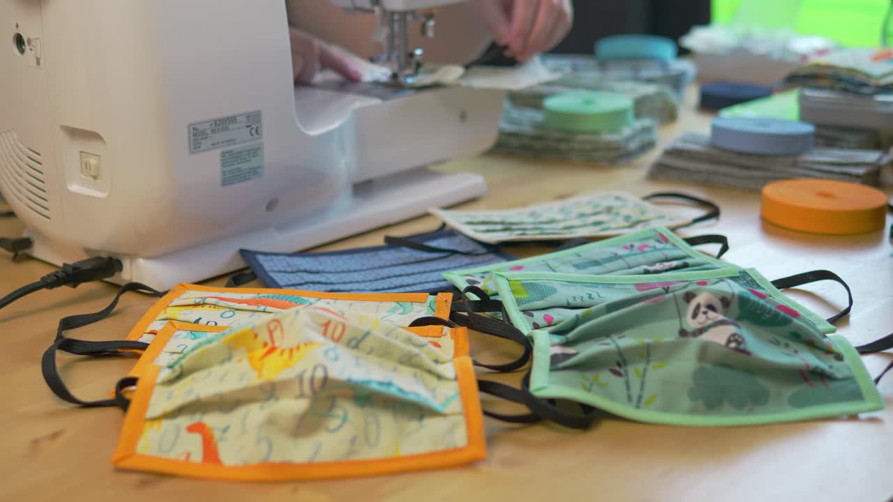 전경에 완성된 마스크가 있는 다양한 다채로운 어린이 디자인의 여성 바느질 얼굴 마스크