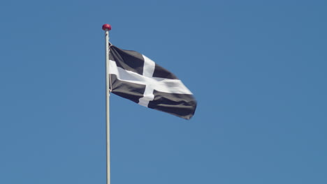 cornwall flag - saint piran's flag on pole waving in the wind with blue sky in the background