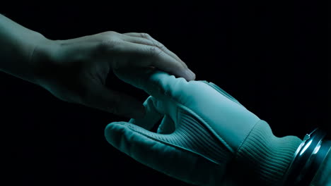 a gloved hand reaches for a bare hand in a dark, futuristic scene