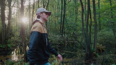 young tall guy with cap walks by a swamplike forest in österlen sweden - tracking profile medium shot