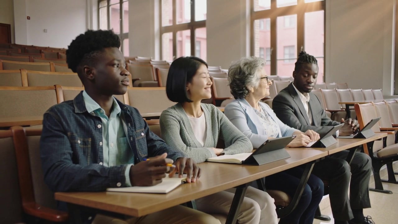 Noticing center woman smiling and looking right, turning peers in class with notes, tablets