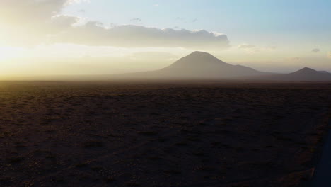 AERIAL---Beautiful-sunrise-on-a-plain-with-a-mountain-peak-in-the-background,-forward