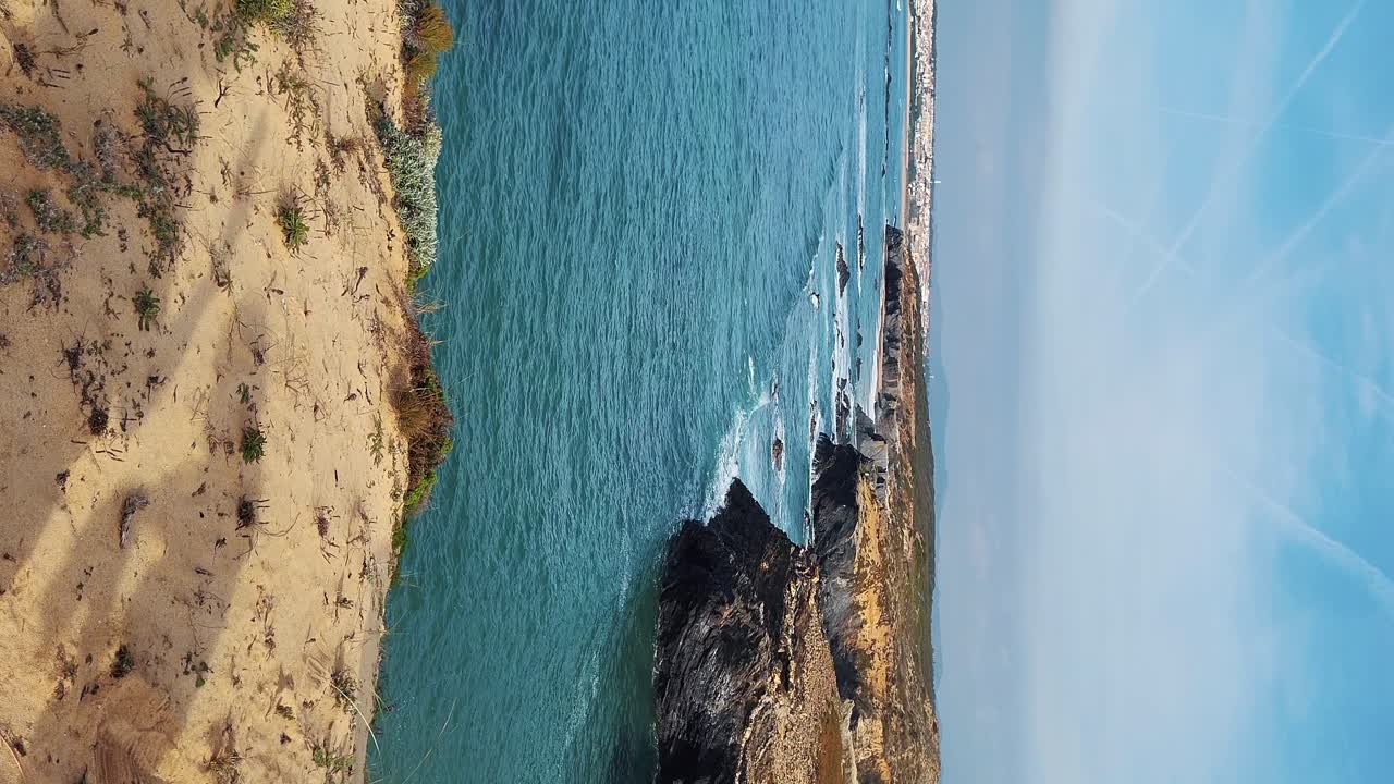 Zambujeira do Mar ved kysten med havbølger, klipper og sandklitter dækket af grøn vegetation, røde blade fra hottentotfigen, solrig dag, klar blå himmel