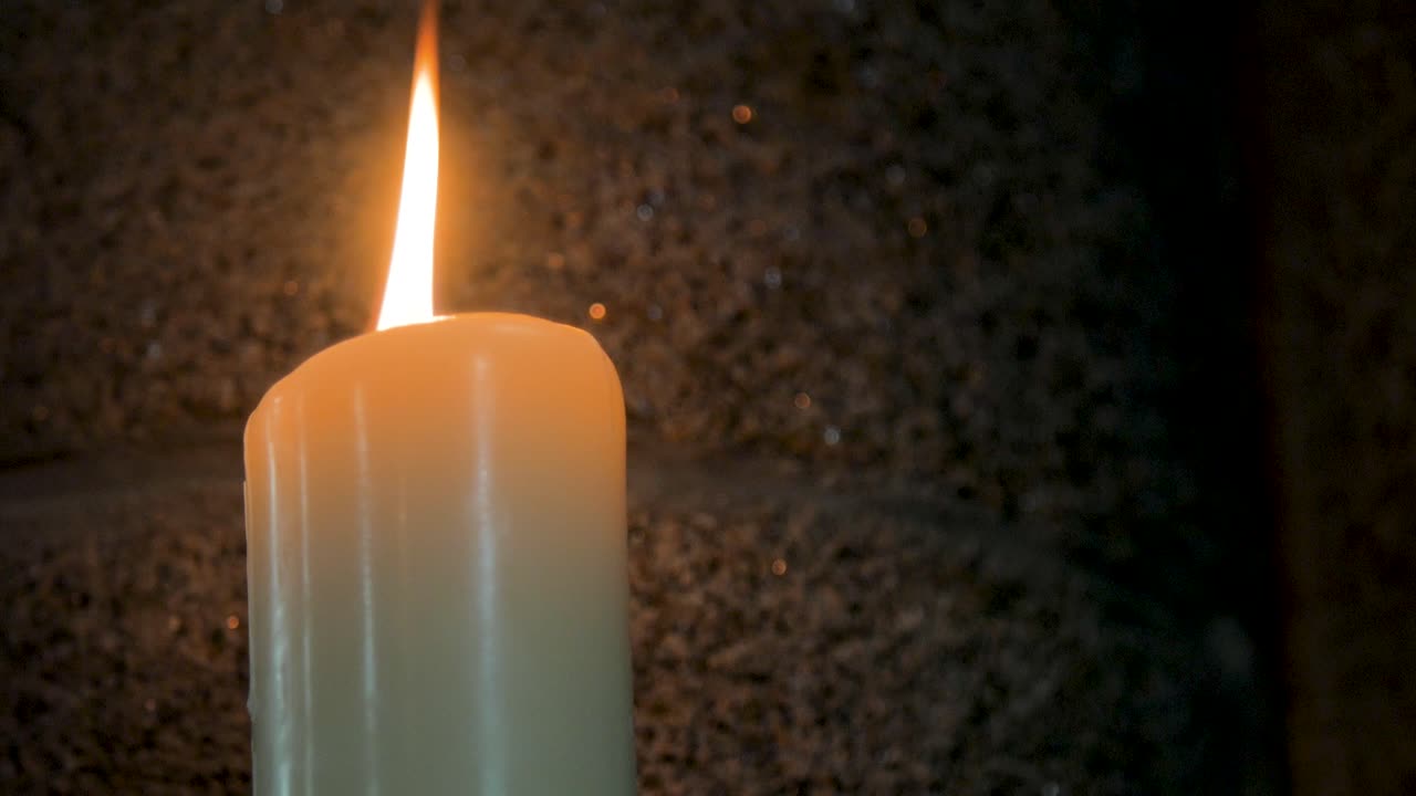 Bougie blanche allumée sur fond de mur en pierre sombre dans une église