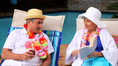 Pareja-Con-Guirnaldas-Junto-A-La-Piscina-Riéndose-De-Un-Libro.