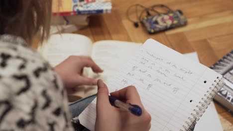 Making-notes-to-paper-notebook---closeup-of-young-female-student