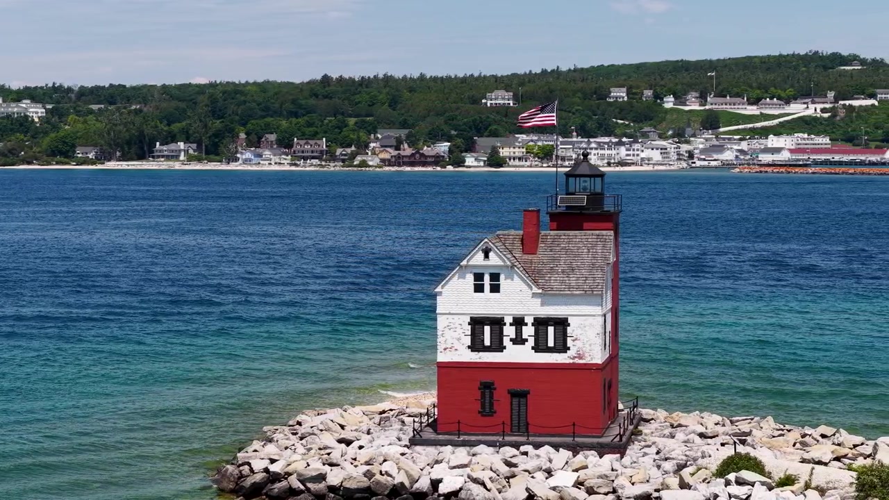 Vista ravvicinata con drone del faro storico di Round Island con acqua turchese e la costa dell'isola di Mackinac sullo sfondo