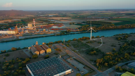 Toma-Aérea-Desde-Arriba-De-Cinco-Turbinas-Eólicas-Cerca-De-Un-Río-En-El-Sur-De-Francia-Al-Atardecer