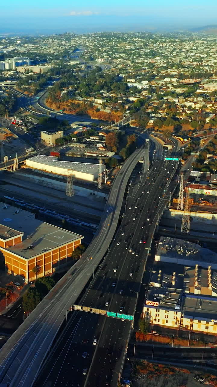 Lively traffic on the highways of Los Angeles at daytime. Sunny panorama of the city at backdrop of mountains. Top view. Vertical video