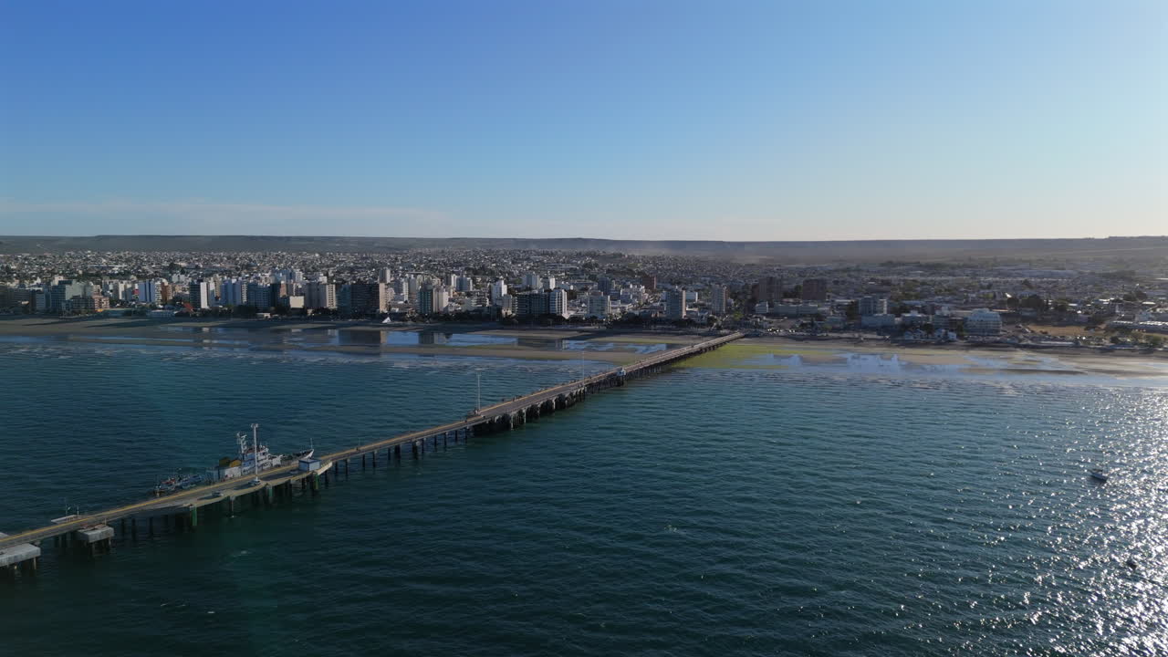 Aerial view of Puerto Madryn Almirante Storni pier reaching the city on a sunny day in Patagonia, Argentina, showing the coastline, the beach, the buildings and the pier