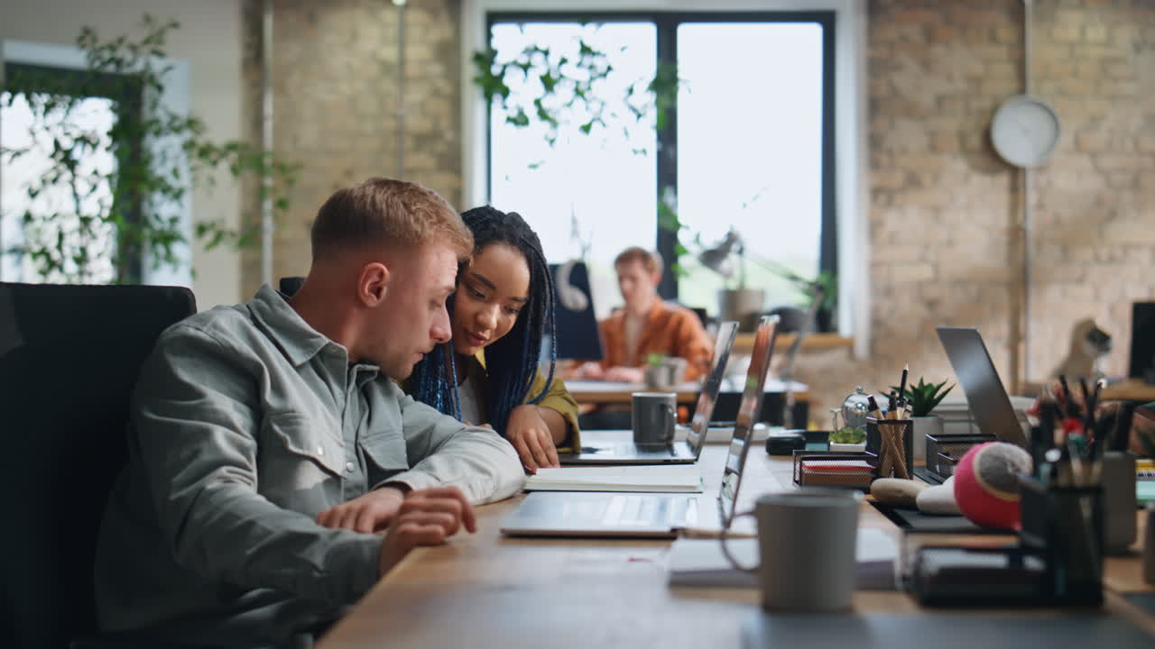 Woman asking advice colleague man sitting workspace. Multiracial team working