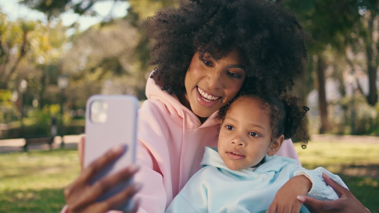 madre hija llamando en video en el teléfono inteligente sentada en la naturaleza soleada de cerca.