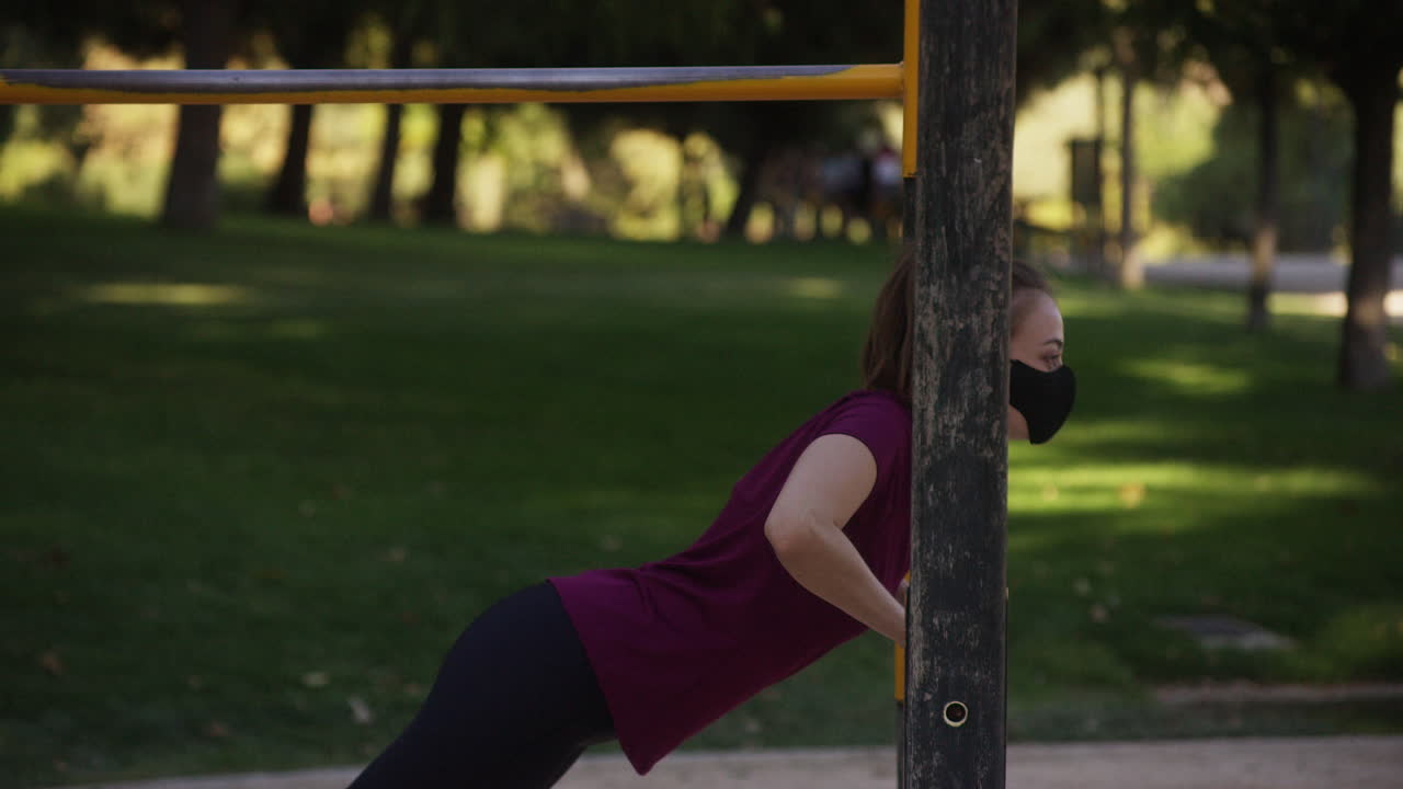 Young woman does incline push ups in a park while wearing a mask, medium shot