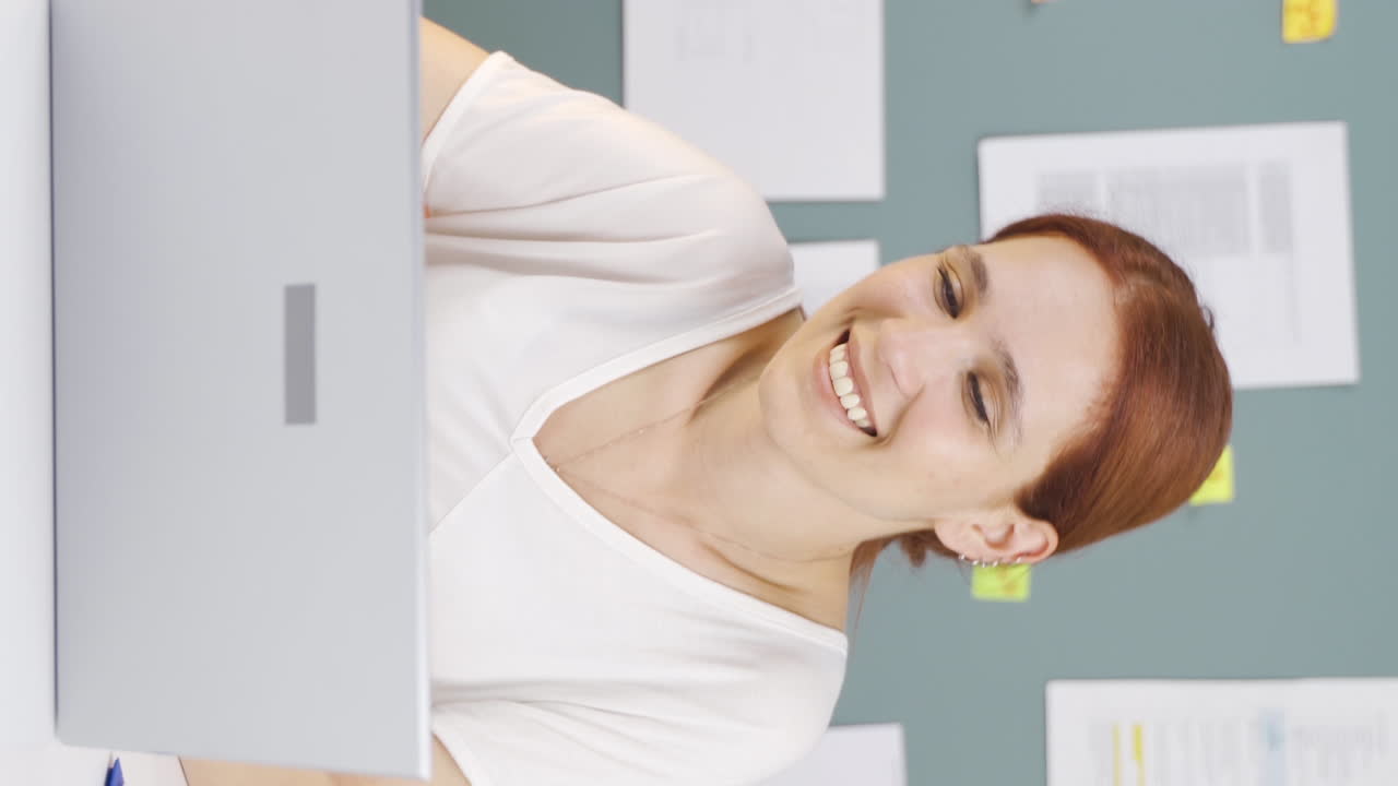 el video vertical de la mujer mirando la computadora portátil es feliz y bailando.