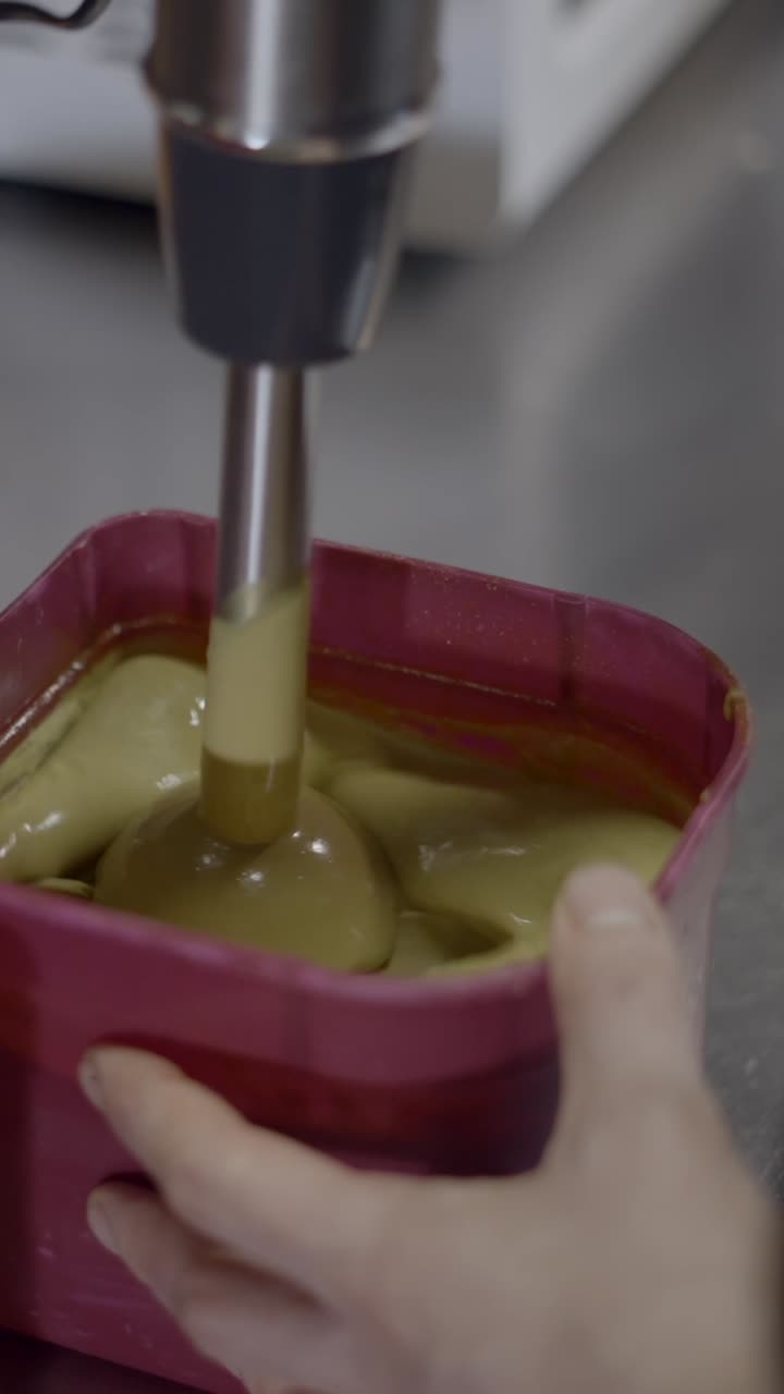 Close-up of an immersion blender mixing a creamy batter in a pink container