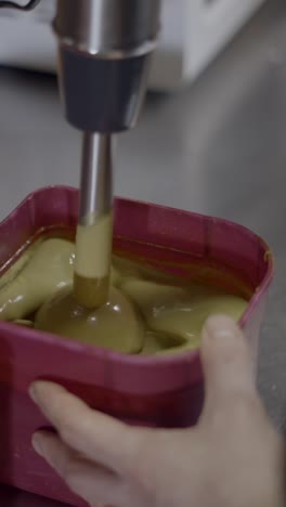 close-up of an immersion blender mixing a creamy batter in a pink container