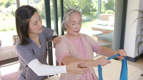 assisting senior woman with resistance band, physical therapist guiding exercise at home