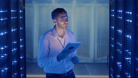 it technician in data center digital server room controlling work of rack server cabinets with a tablet. professional server engineer at work.