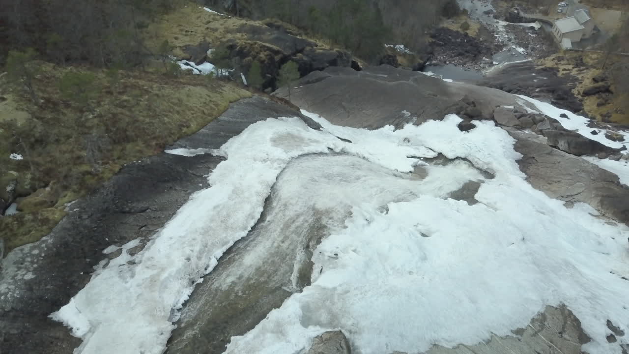 vista de drones volando sobre una cascada cortando la nieve derretida circundante, inclinación lenta hacia abajo