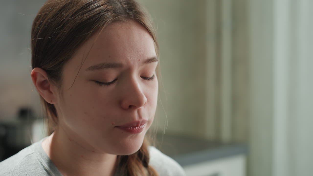 Pregnant woman experiencing intense nausea, closeup. Teary eyes and sweating forehead, slow breathing to ease discomfort, muted morning light in domestic kitchen, intimate vulnerable portrait showing
