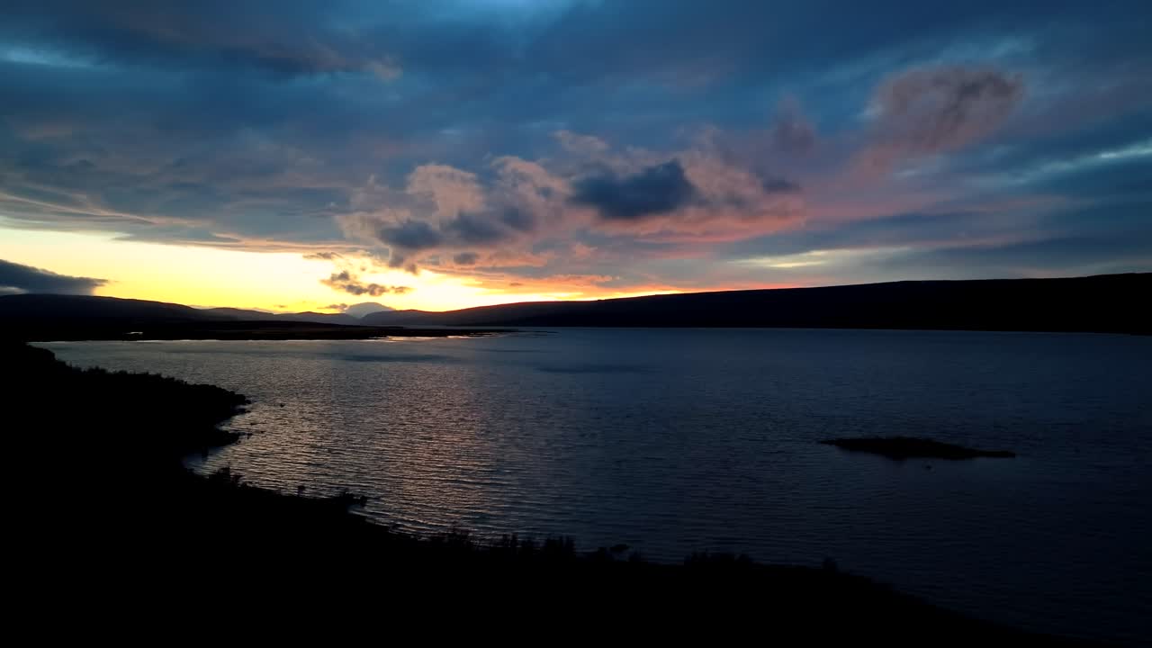 Colorful sunset over Lagarfljot River near Egilsstaðir Iceland as a couple in silhouette walks by as the drone descends