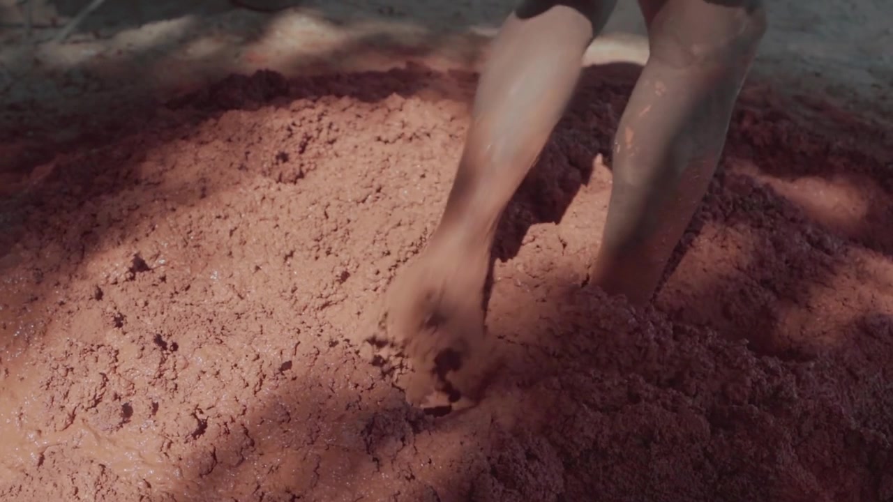 Barefoot indigenous people stomping and mixing clay with their feet. A traditional method of preparing mud for natural building in Brazil