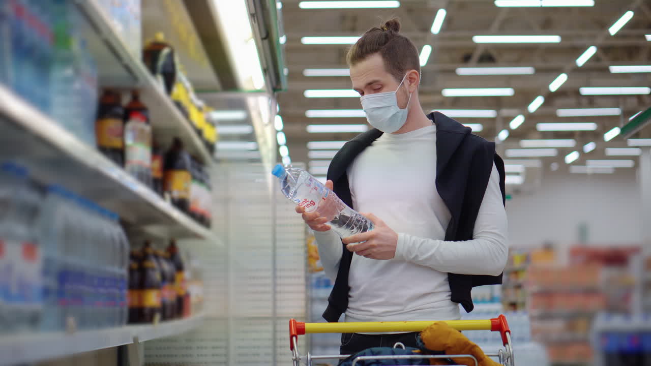 Man shopping for water bottles in a supermarket wearing a mask during the pandemic