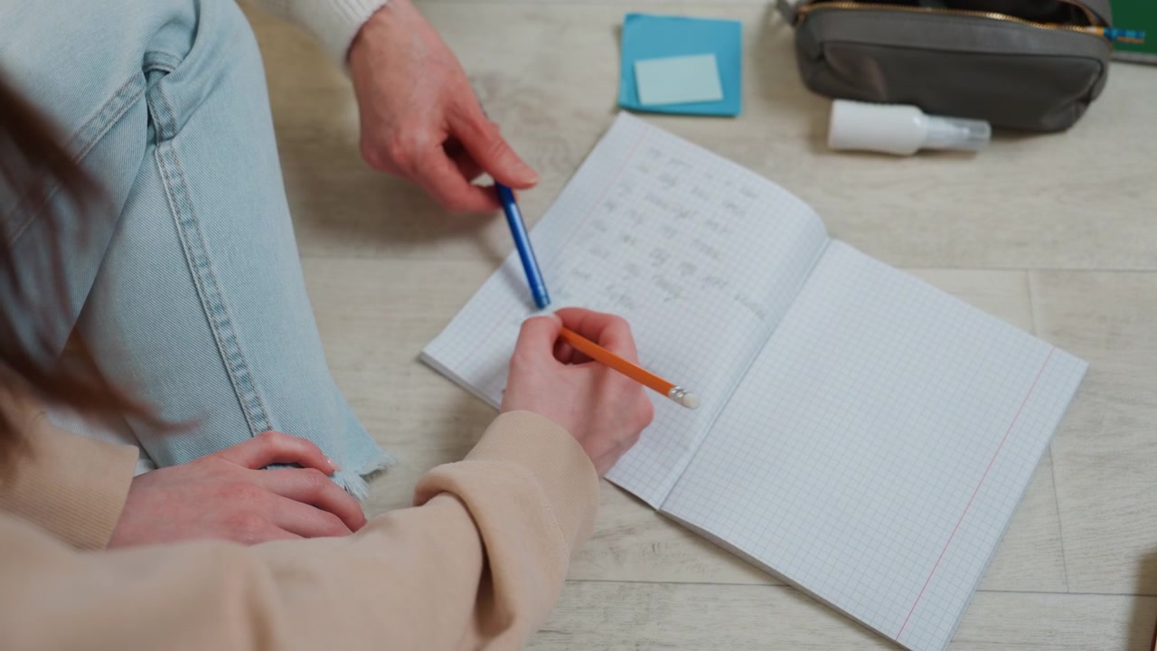 Student practicing grammar exercises in notebook, pencil and tutor hand pointing at sentences, cozy living room floor, soft natural light, casual clothes, focused guidance and corrective feedback